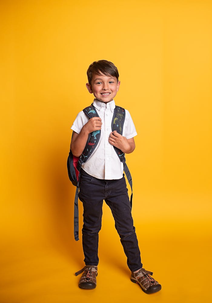 Young boy standing with a backpack, ready for school on yellow background.